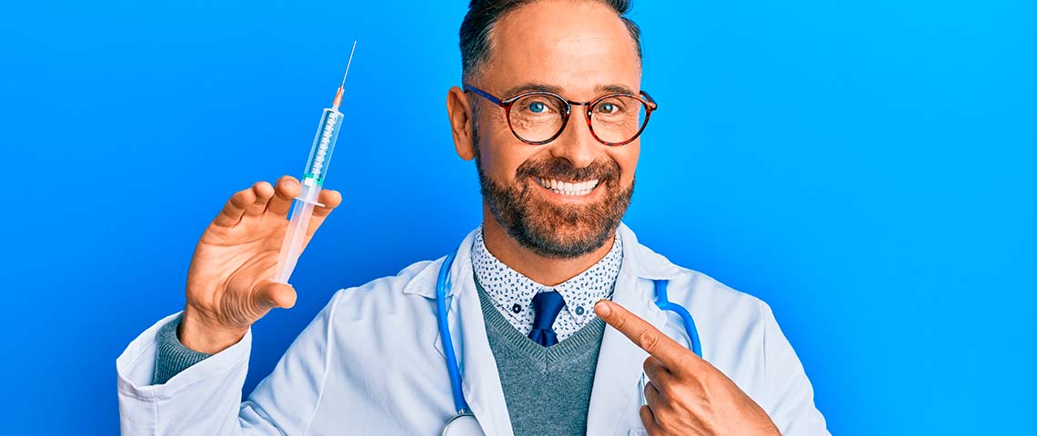 мужчина врач указывает пальцем на шприц, который держит в другой руке